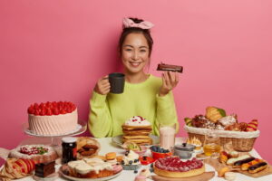 Woman holds cake sitting in behind table full of sweets